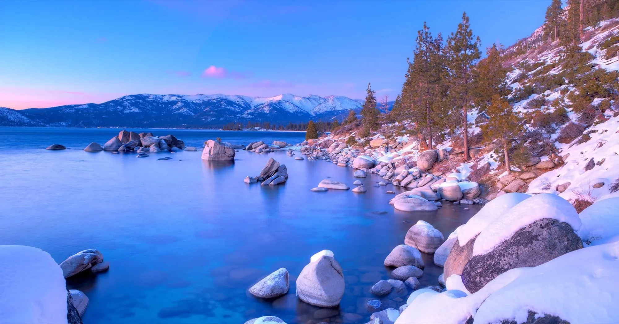 Snow-covered boulders and pines beside Lake Tahoe